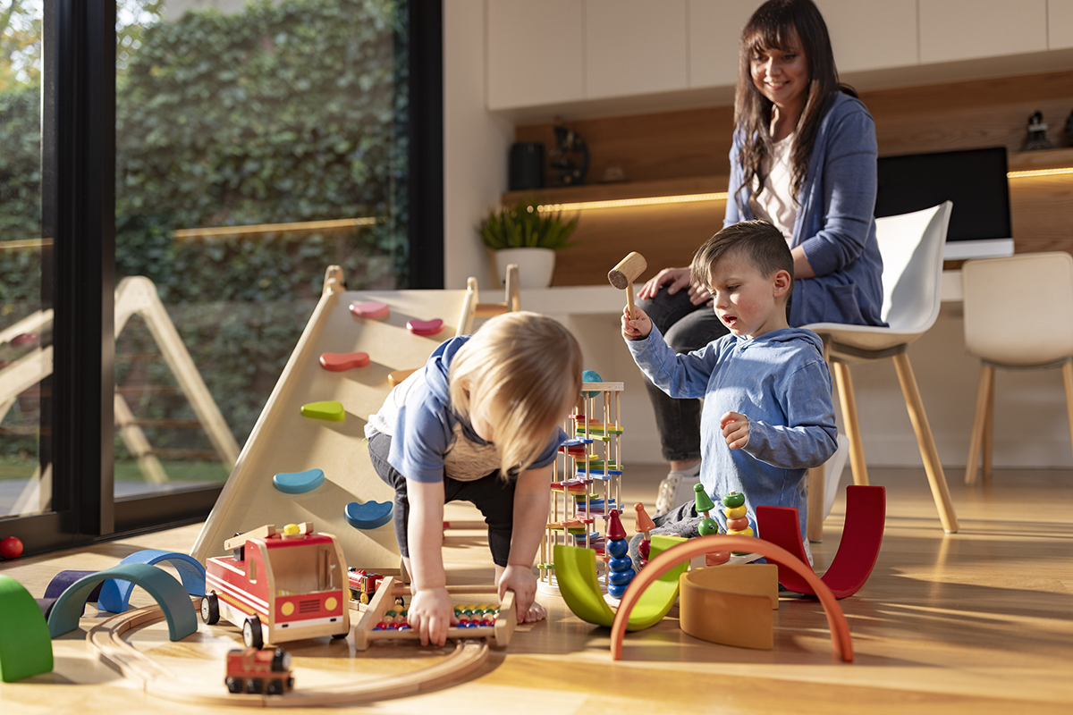 Photo of mother watching her two young children play with wood toys